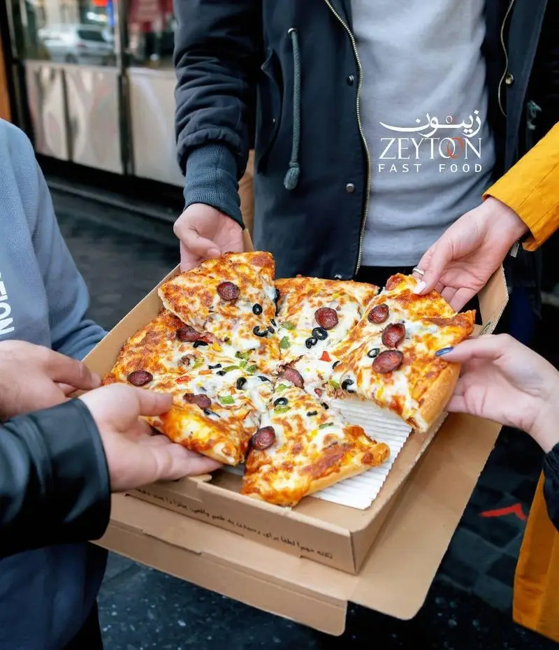 گروهی از افراد در حال لذت بردن از پیتزای داغ و خوشمزه رستوران فست فود زیتون، بهترین انتخاب برای دورهمی‌های شما با طعم‌های فراموش‌نشدنی.