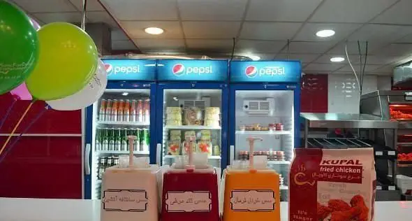 فضای داخلی رستوران فست فود مرغ سوخاری کوپال، شامل یخچال‌های پپسی پر از نوشیدنی، سس‌های مخصوص و بسته مرغ سوخاری آماده.