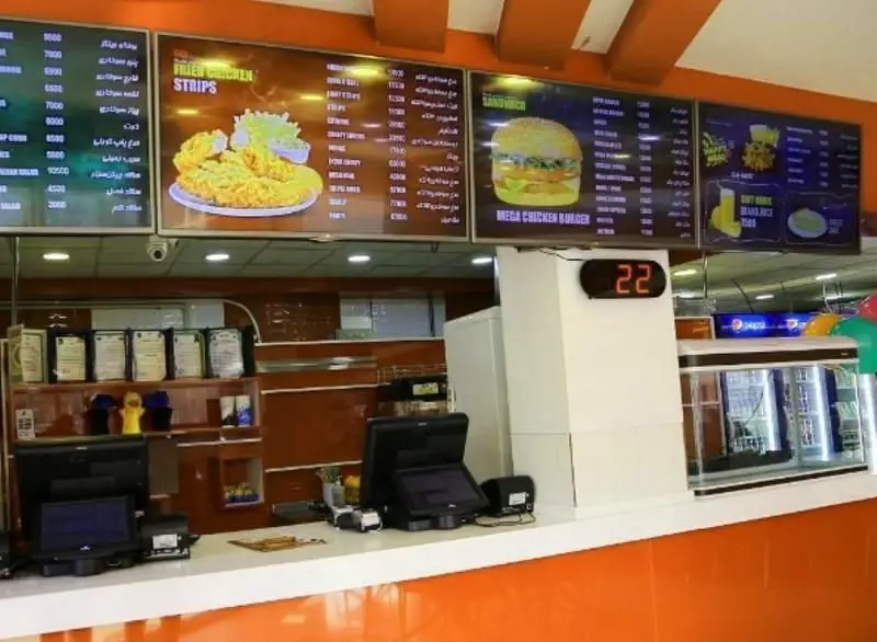 نمای داخلی فست فود مرغ سوخاری کوپال: نمایشگرهای منوی دیجیتال غذاها شامل مرغ سوخاری، ساندویچ و برگر در کنار پیشخوان سفارش و دستگاه‌های پوز.