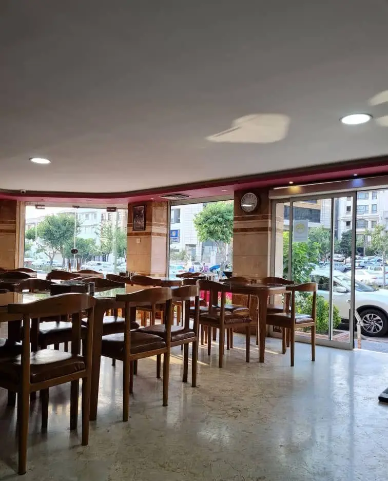 نمایی از سالن غذاخوری جگرکی کبابی شاطر میرزا با چیدمان میز و صندلی چوبی و پنجره‌های بزرگ رو به خیابان شهر.