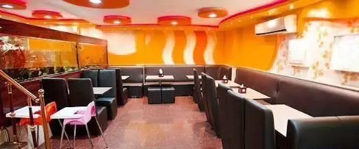 فضای داخلی جذاب و مدرن رستوران پیتزا مکروم با دیوارهای نارنجی، نیمکت‌های راحت مشکی و میزهای تمیز، محیطی ایده‌آل برای لذت از بهترین پیتزاها.