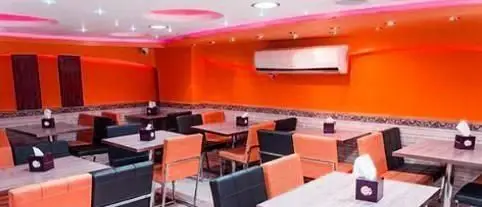 فضای داخلی رستوران پیتزا مکروم با دکوراسیون نارنجی روشن، میز و صندلی‌های تمیز و مدرن برای تجربه‌ای دلنشین.