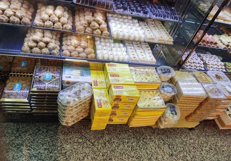 شیرینی‌فروشی آنا: ویترین شلوغی از انواع شیرینی تازه و خوشمزه شامل باقلوا، کلوچه و دیگر شیرینی‌های سنتی آماده سفارش برای مشتریان عزیز.