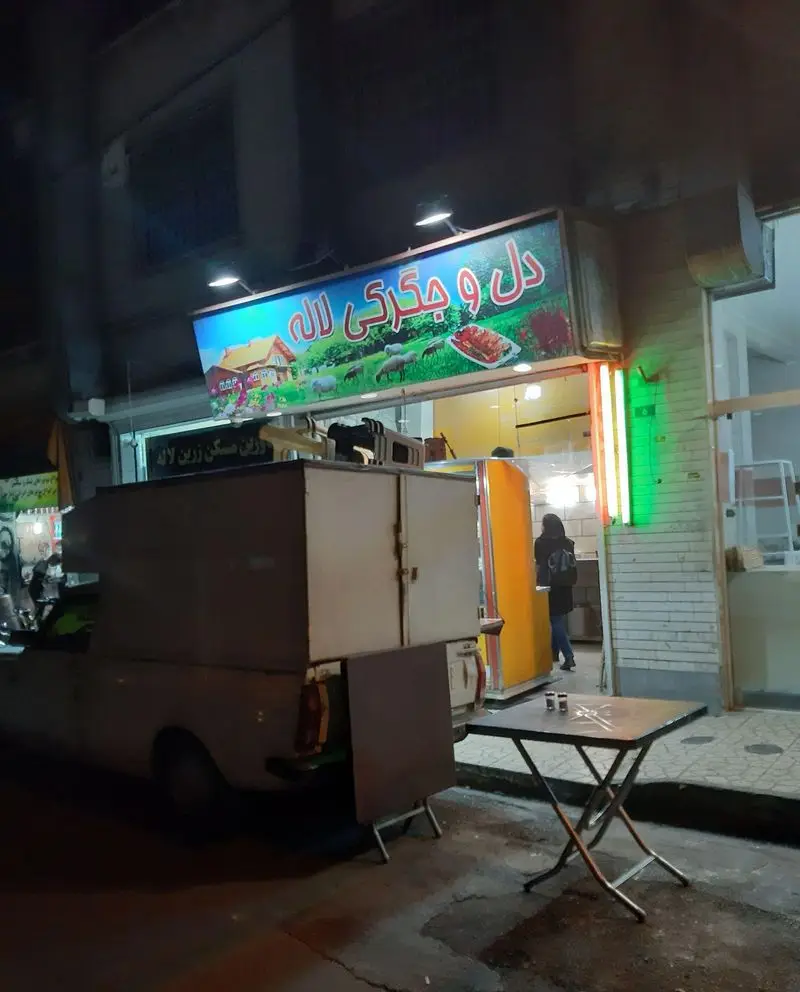 تصویری در شب از کسب و کار دل و جگرکی لاله، با تابلوی درخشان و تصویر کباب، محیط پذیرایی بیرونی و وانت مخصوص