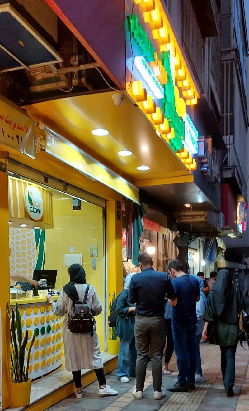 مشتریان در حال خرید ذرت مکزیکی تازه و خوشمزه از مغازه سه نقطه واقع در کارگر شمالی تهران، با محیطی دلپذیر.