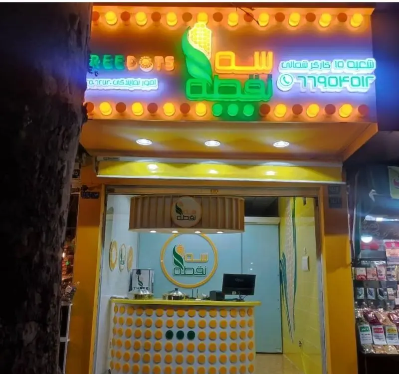 مغازه فست فود ذرت مکزیکی سه نقطه در کارگر شمالی تهران، با تابلوی نئون و لوگوی جذاب ذرت و ترکیب رنگ زرد و سبز.