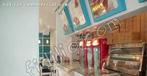 فضای داخلی مدرن فست فود سفید آبی: پیشخوان آماده‌سازی، یخچال‌های نوشابه قرمز، منوهای پیتزا و برگر با قاب آبی و جعبه‌های پیتزا.