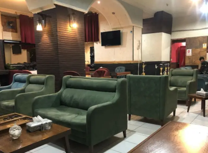 فضای داخلی کافه سنتی نارنج با مبلمان سبز راحت، میزهای چوبی و قلیان‌های آماده، محیطی دنج و دلنشین برای مشتریان.