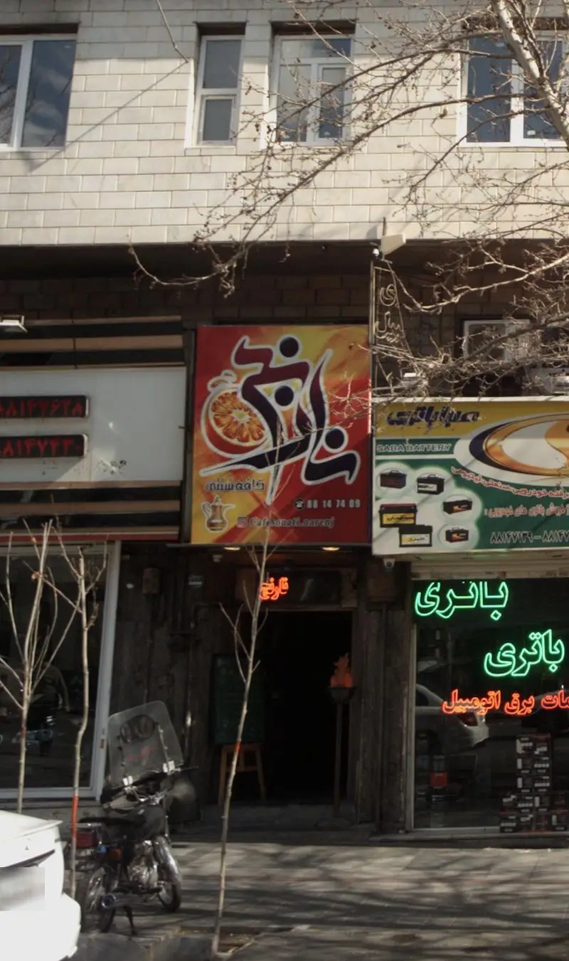 نمای بیرونی کافه سنتی نارنج با تابلوی رنگارنگ شامل نام کافه، برش پرتقال، و قوری در کنار سایر کسب و کارهای شهری