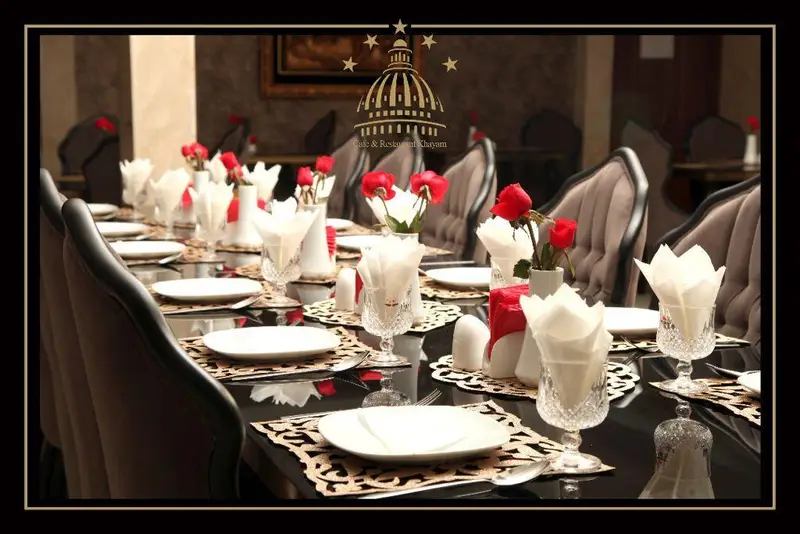 تصویری از میز بلند و باشکوه مجموعه پذیرایی و رستوران خيام با چیدمان لوکس، گلدان‌های گل رز و ظروف کریستال برای مهمانان.