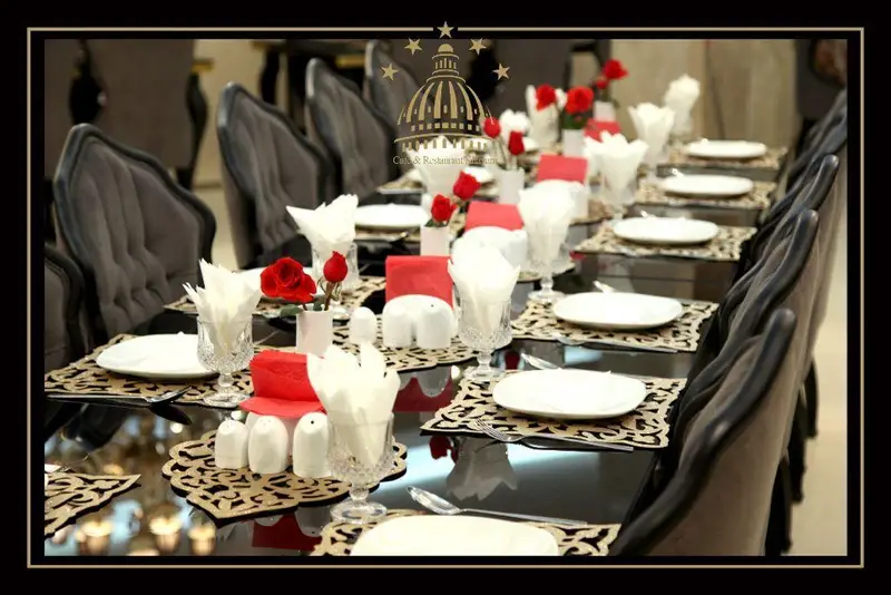 نمایی از میز شام مجلل و بلند با چیدمان کامل، صندلی‌های شیک و گل‌های رز قرمز در مجموعه پذیرایی خيام برای مهمانی‌ها و جشن‌ها.