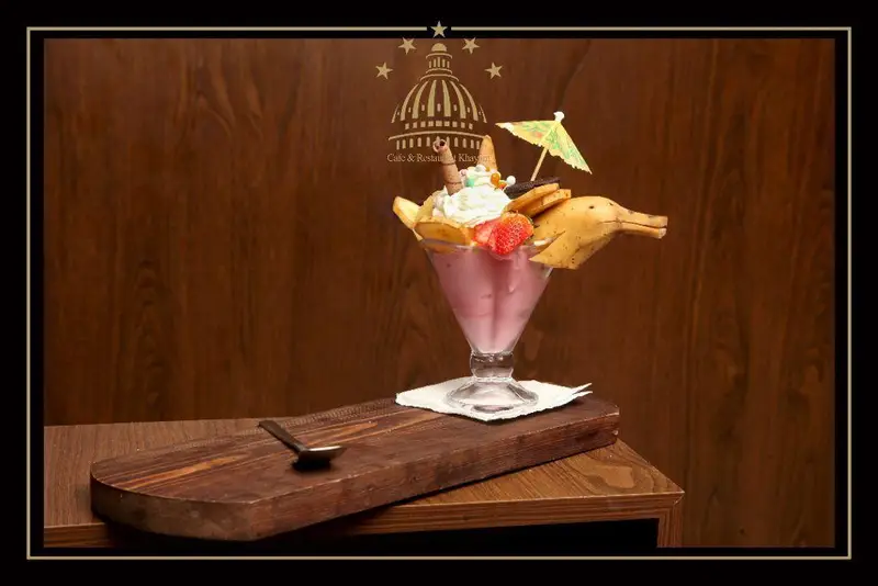 یک میلک شیک صورتی خلاقانه و خوشمزه با خامه، توت فرنگی و تزئین موز دلفینی در کافه و رستوران مجموعه پذیرایی خیام.