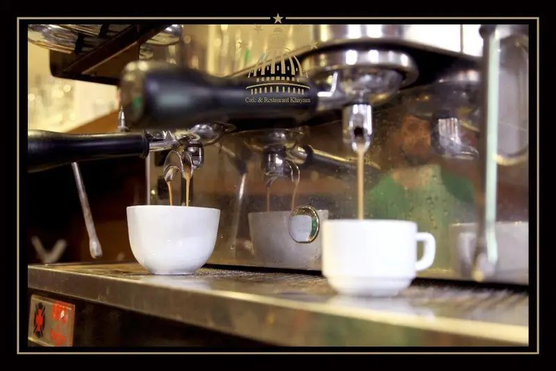 تصویری جذاب از دستگاه اسپرسو در حال ریختن قهوه تازه و داغ در فنجان‌های سفید در کافه رستوران مجموعه پذیرایی خیام