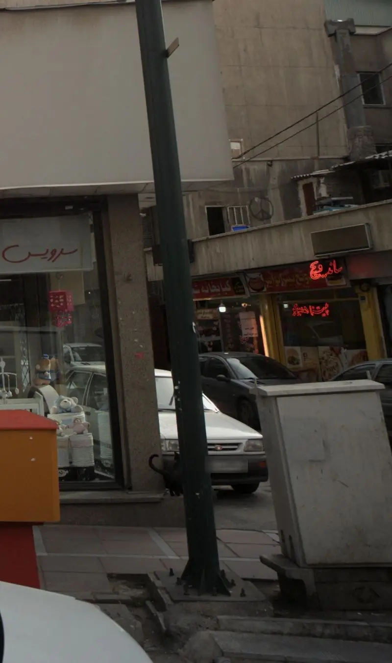 نمای خیابانی فست فود ساندویچ و پیتزا توانیر در منطقه توانیر تهران، با تابلوهای روشن و تردد خودروها در محیط شهری.