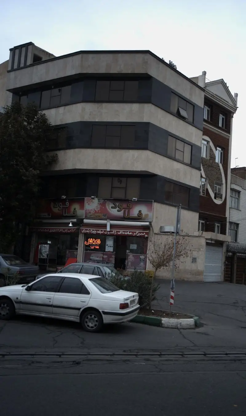 نمای بیرونی فست فود فلافود اصفهان، با ارائه انواع ساندویچ، همبرگر، پیتزا و هات‌داگ. محیط شهری با ساختمان‌ها و خودروها.