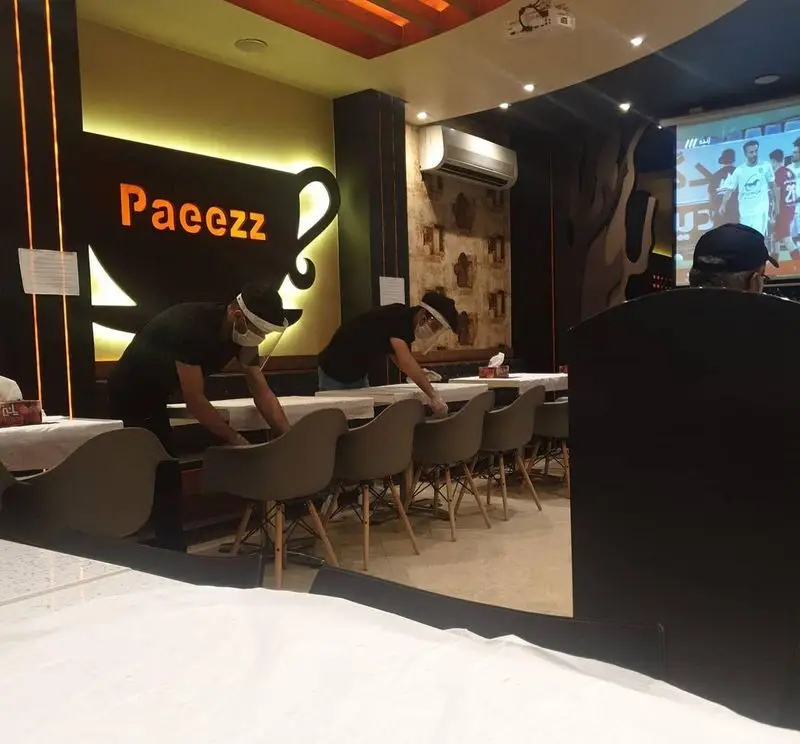 محیط بهداشتی و آماده پذیرایی از مشتریان فست فود پاییز (Paeezz) با کارکنانی در حال نظافت و نمایش فوتبال.