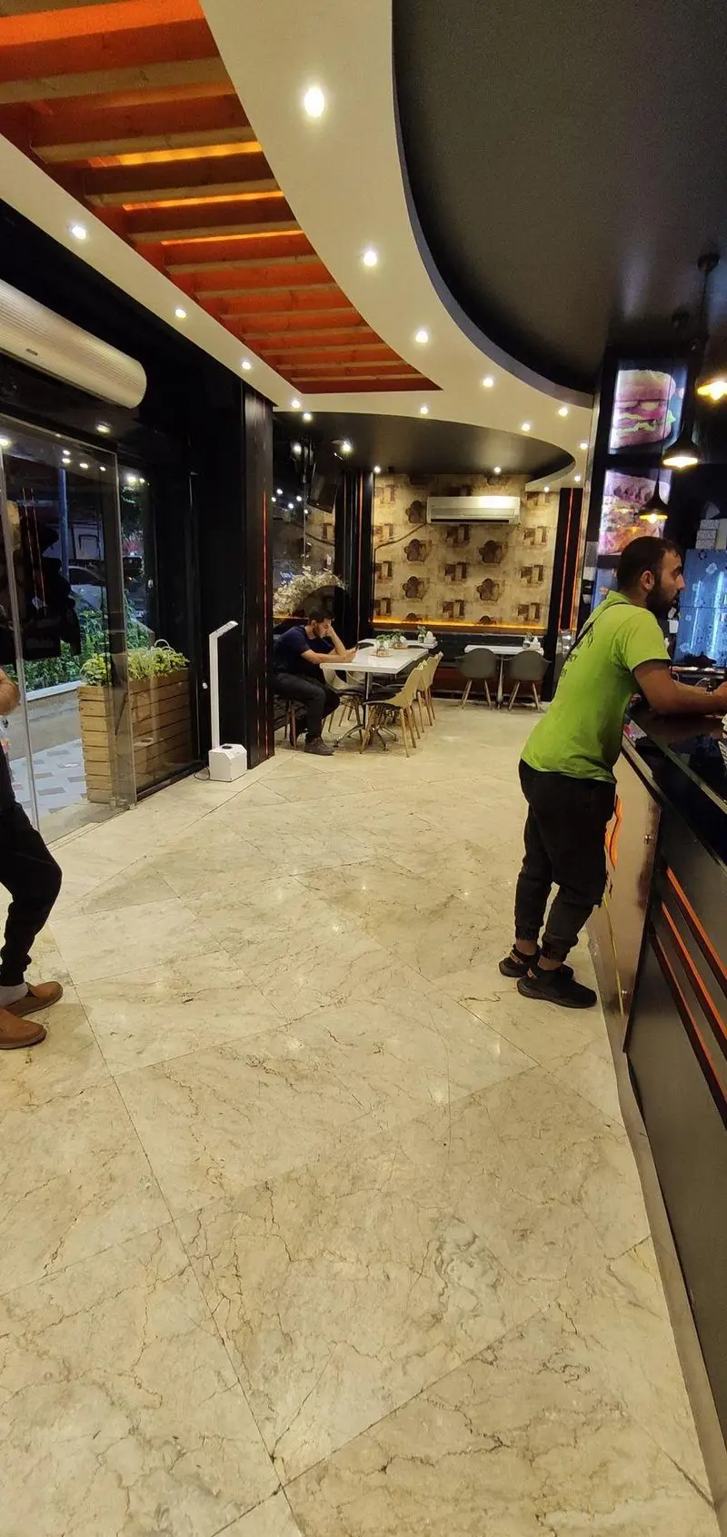 نمایی داخلی از فست فود پاییز با دکوراسیون مدرن، سقف چوبی و نورپردازی زیبا. مشتریان و پرسنل در فضای تمیز و دنج رستوران.