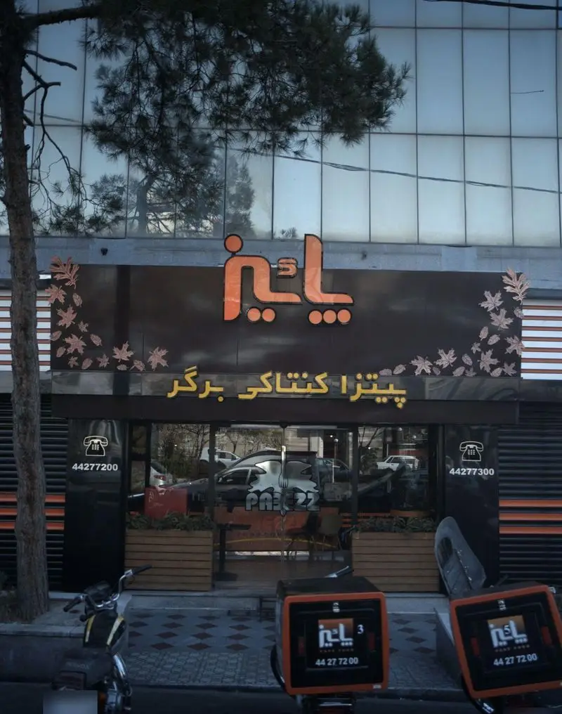 فست فود پاییز: نمای بیرونی شعبه با تابلوی بزرگ پیتزا، کنتاکی و برگر. شامل باکس‌های تحویل غذا، شماره تماس و لوگوی پاییز برای سفارش آنلاین.