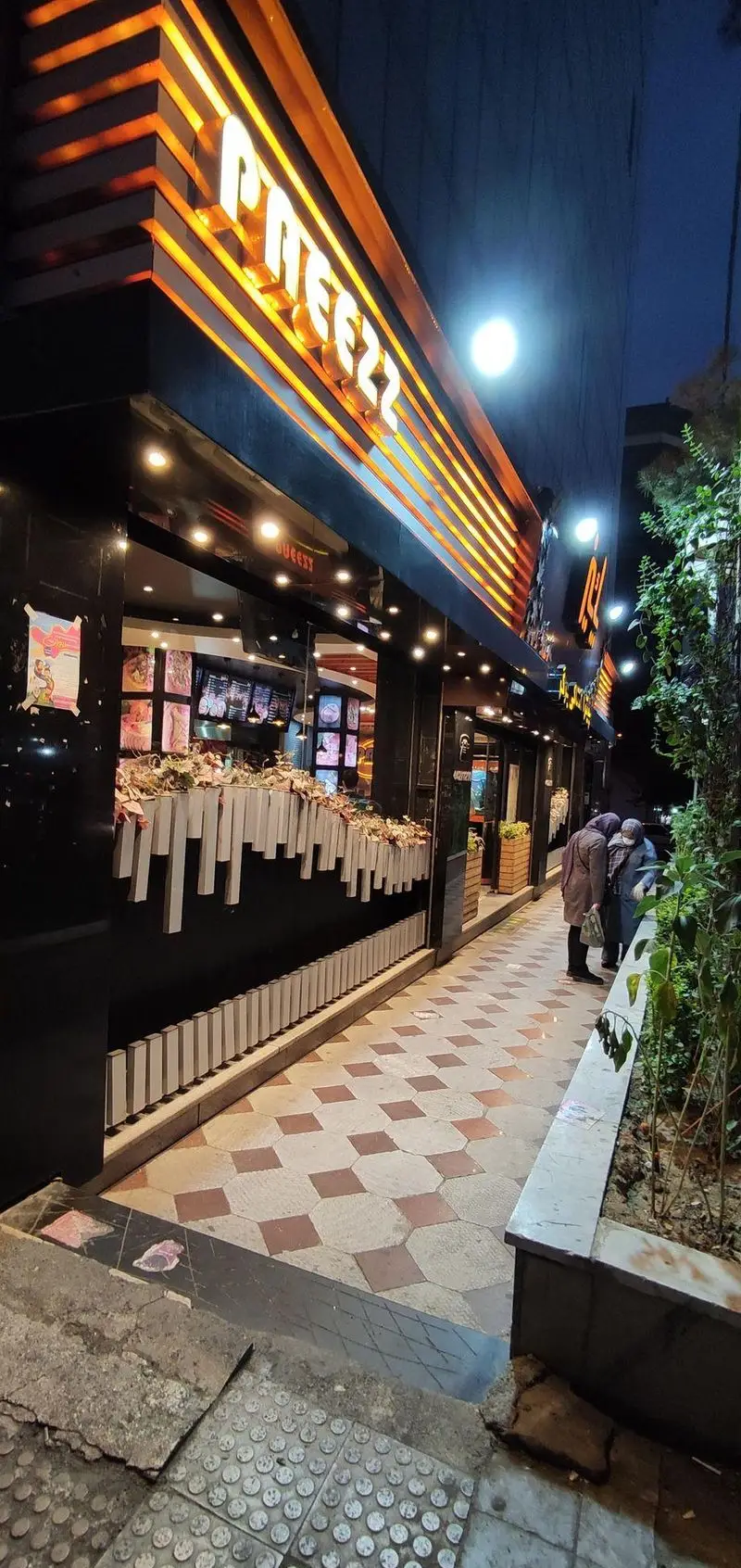 نمای بیرونی جذاب فست فود پاییز در شب، با تابلوهای درخشان نارنجی و دکوراسیون مدرن، پذیرای مشتریان با بهترین غذاها.