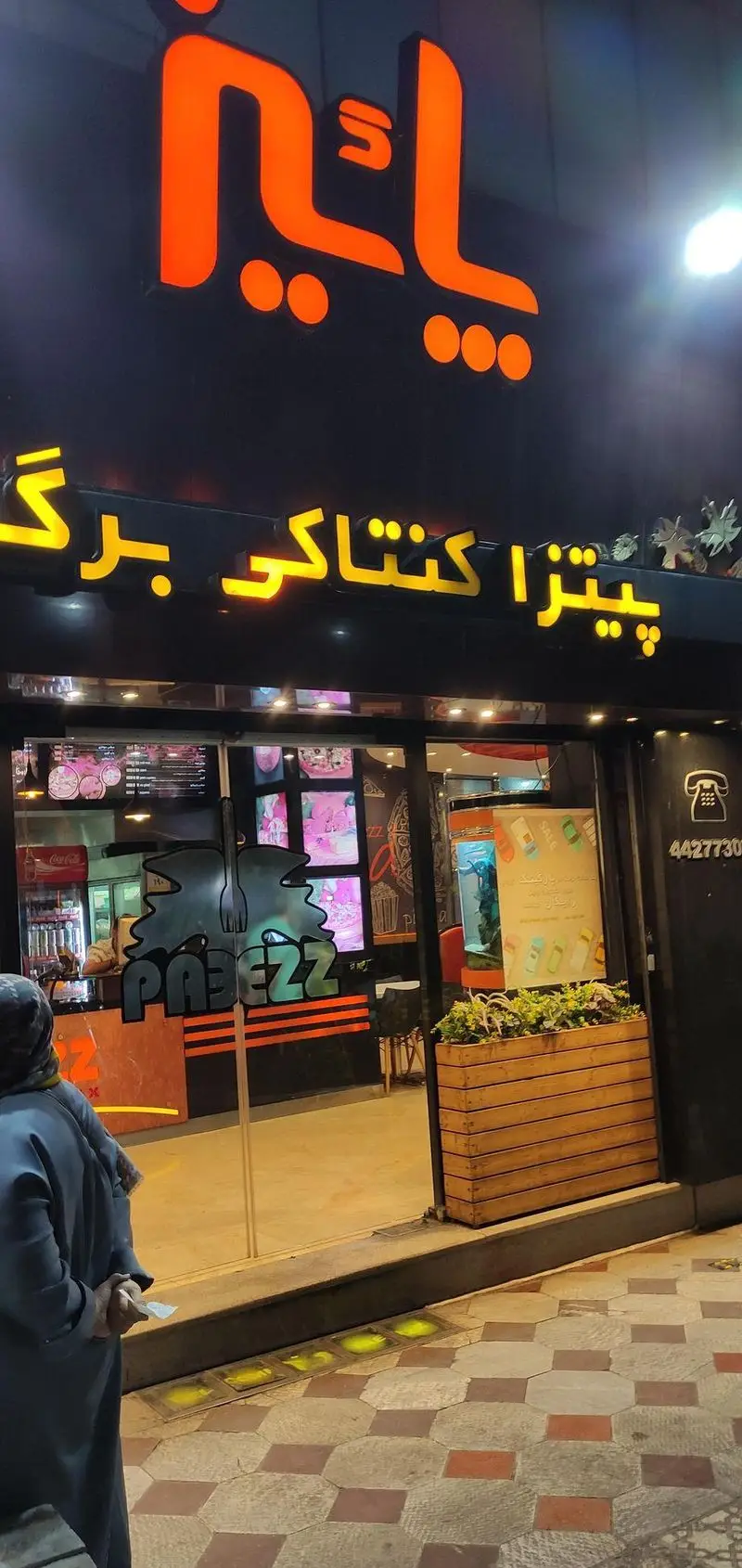 ورودی فست فود پاییز (Paeez Fast Food) با تابلوی نئونی درخشان. ارائه دهنده پیتزا، کنتاکی و برگر. شامل شماره تماس 44277300 و دکوراسیون داخلی.