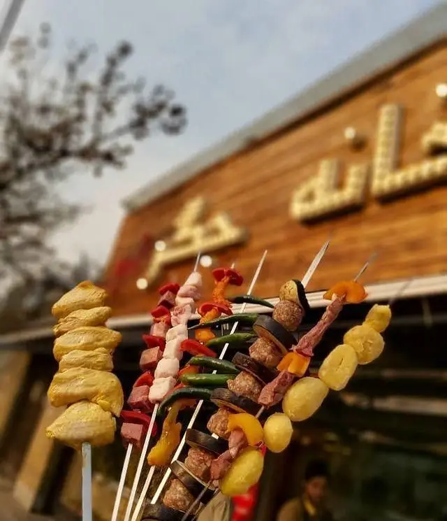 تصویری از سیخ‌های متنوع کباب شامل جگر، مرغ، گوشت و سبزیجات در مقابل رستوران خانه جگر، ارائه دهنده غذاهای سنتی ایرانی.