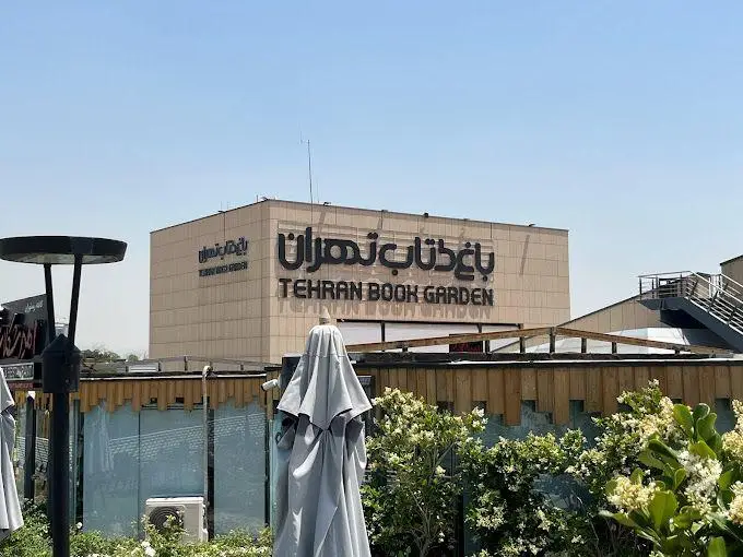 باغ کتاب تهران: نمایی از ساختمان اصلی و فضای باز با چترها و درختان. مقصدی جذاب برای دوستداران کتاب و فرهنگ در تهران.