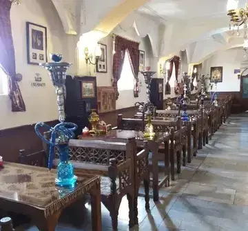 فضای داخلی وسیع و دلنشین سفره خانه سنتی پرستو با ردیف‌های میز و صندلی چوبی، دکوراسیون اصیل ایرانی و قلیان‌های متنوع برای مشتریان.