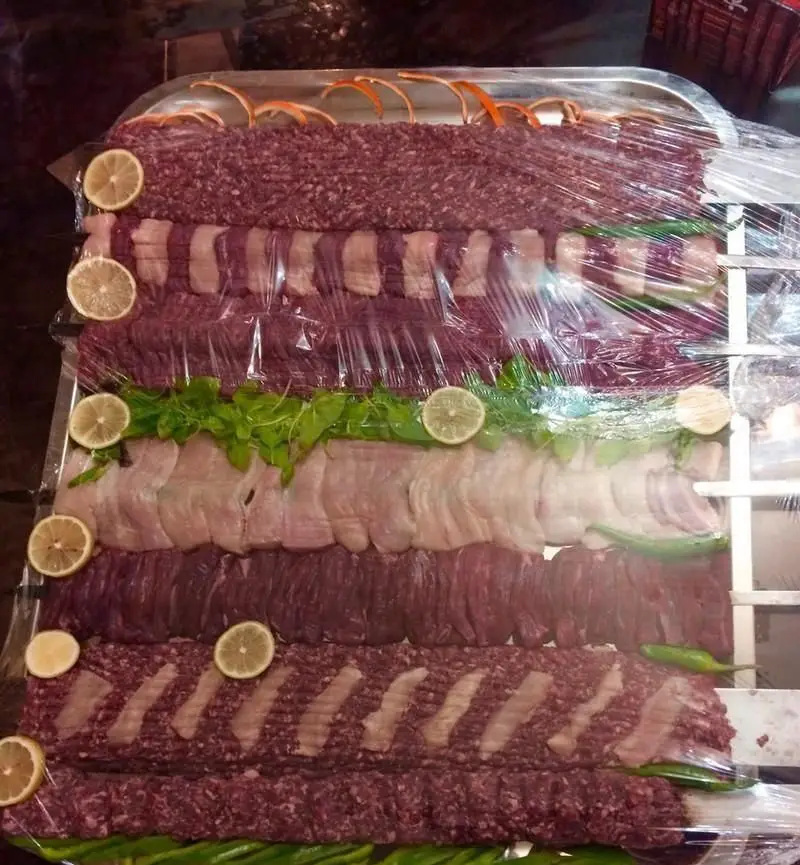 انواع کباب‌های تازه و آماده پخت (کوبیده، برگ، جوجه) روی سیخ همراه با لیمو و سبزیجات در رستوران ایرانی قدح.