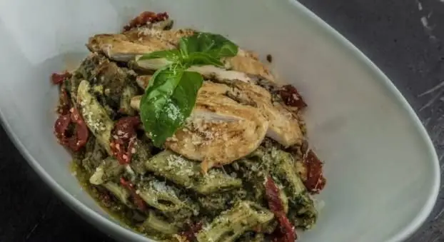 تصویری از پاستا پنه پستو با مرغ گریل، گوجه خشک و پنیر پارمزان، تزیین شده با ریحان در رستوران ایتالیایی بونو.