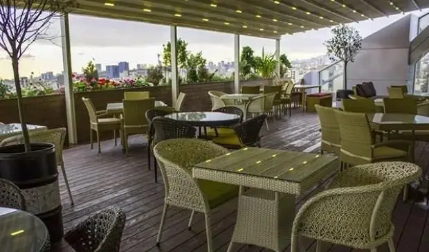 نمای زیبای فضای باز رستوران ایتالیایی بونو با تراس روف گاردن، میز و صندلی‌های حصیری، چشم‌انداز شهری دلنشین و دکوراسیون گیاهی.