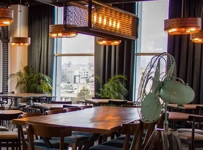 فضای داخلی دلنشین و شیک رستوران ایتالیایی بونو با میزهای چوبی بزرگ، نورپردازی صنعتی خاص، گیاهان سبز و چشم‌انداز بی‌نظیر شهر.