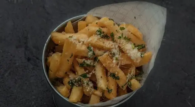 سیب‌زمینی سرخ‌کرده طلایی و ترد، با پنیر پارمزان رنده شده و جعفری تازه، سرو شده در سطل فلزی. غذای جانبی محبوب رستوران ایتالیایی بونو.