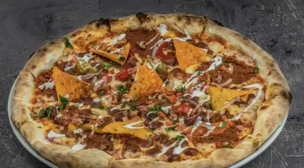 پیتزا مکزیکی لذیذ با گوشت طعم‌دار، پیاز، فلفل هالوپینو، سس سیر و چیپس ناچو در رستوران ایتالیایی بونو. طعمی جدید برای شام.