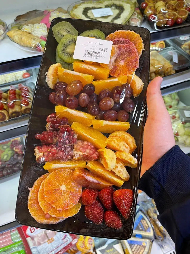 سینی میوه خرد شده تازه و آماده شامل کیوی، پرتقال، انگور، انار و توت فرنگی در سوپر پروتئین ملل برای خرید آسان.