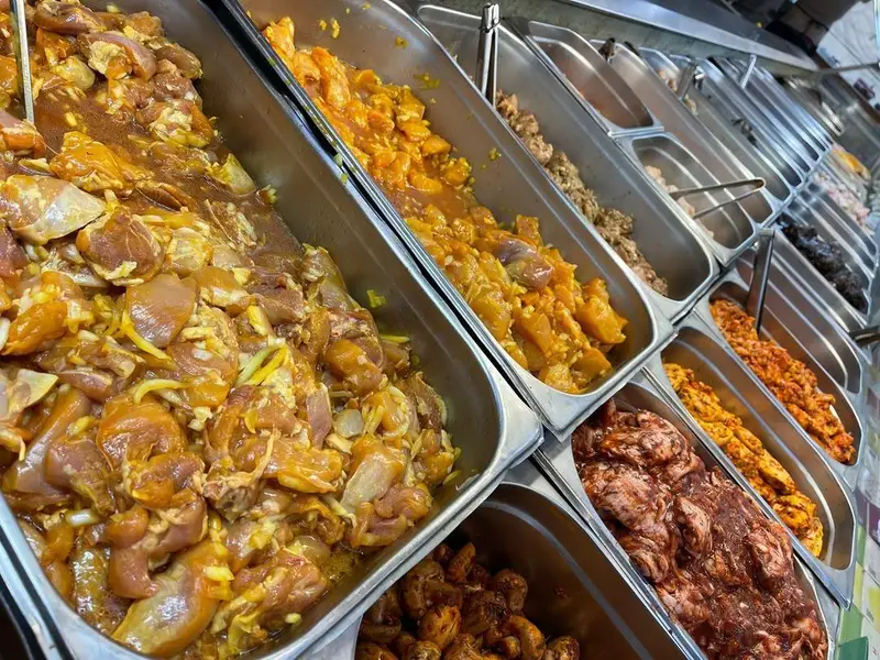 سینی‌های بزرگ پر از انواع گوشت و مرغ طعم دار شده و آماده طبخ، محصولات پروتئینی تازه در سوپر پروتئین ملل.