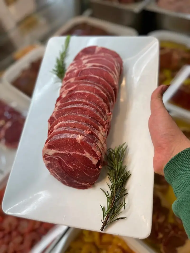 سینی بزرگ گوشت قرمز گوساله تازه و برش خورده با رزماری سبز، محصول باکیفیت سوپر پروتئین ملل برای طبخ انواع استیک و کباب.