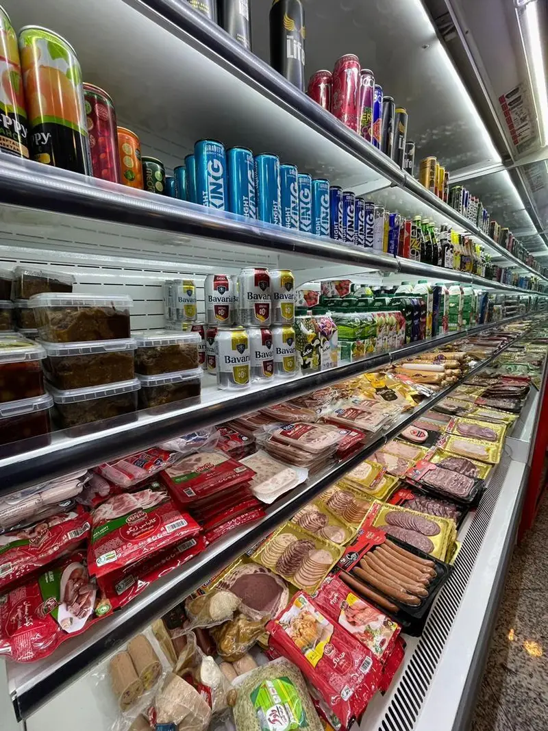 راهروی یخچال سوپر پروتئین ملل با قفسه‌های پر از سوسیس، کالباس، انواع محصولات پروتئینی بسته‌بندی‌شده، و نوشیدنی‌های متنوع.