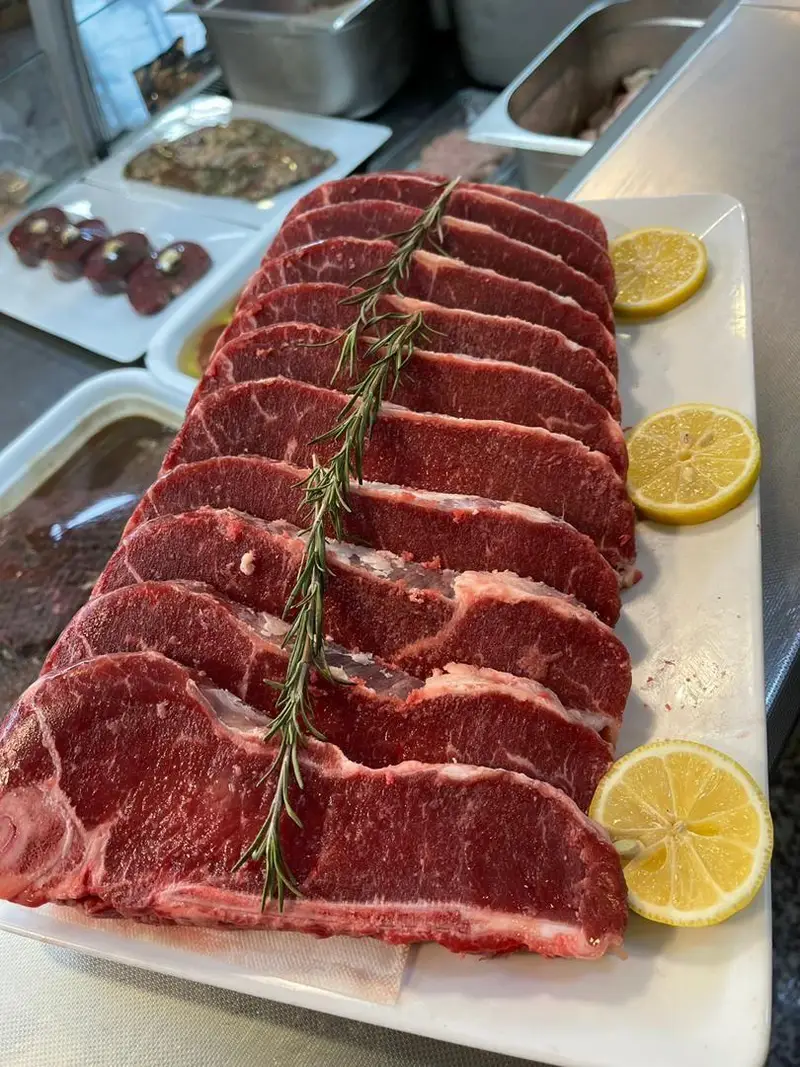 بشقاب بلند حاوی تعداد زیادی برش گوشت قرمز تازه (استیک) با تزئین رزماری و لیمو در سوپر پروتئین ملل. پروتئین باکیفیت.