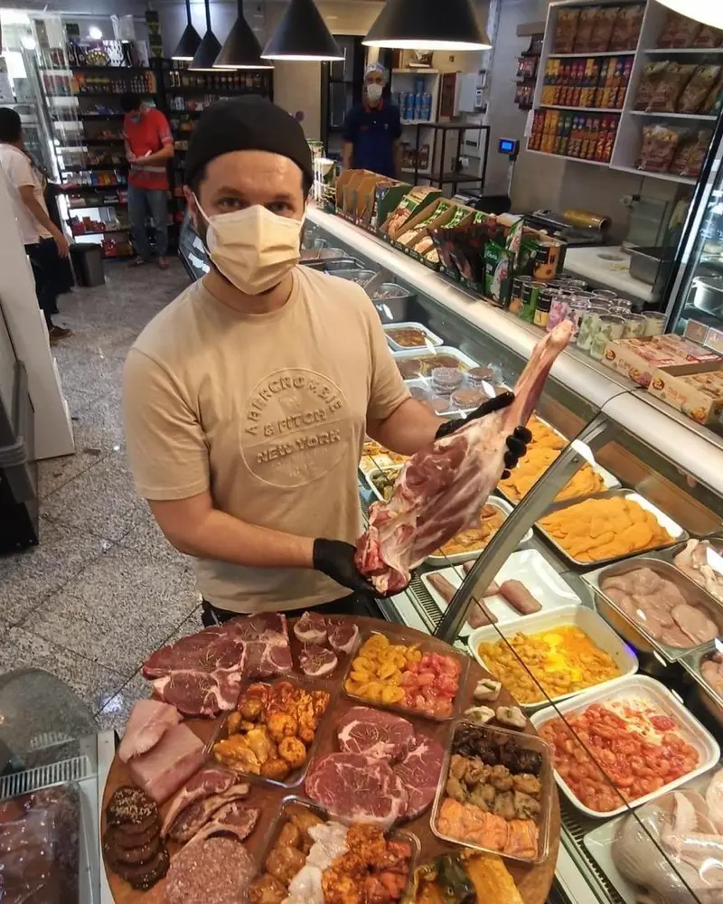 قصاب سوپر پروتئین ملل در فروشگاه، ران بره تازه را نشان می‌دهد، با تنوع بی‌نظیر محصولات گوشتی و پروتئینی.