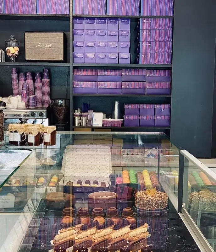 دکوراسیون داخلی کافه لوندر با قفسه‌های پر از جعبه‌های شیرینی، ماکارون‌های رنگی، انواع کیک و دسر و تجهیزات آماده‌سازی قهوه.