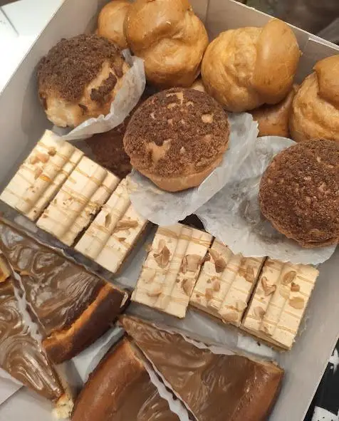 تصویری از یک جعبه پر از شیرینی‌های لذیذ گلستان: نان خامه‌ای، شیرینی کراکلین، دسرهای کاراملی و تارت‌های مغزدار برای جشن‌ها.