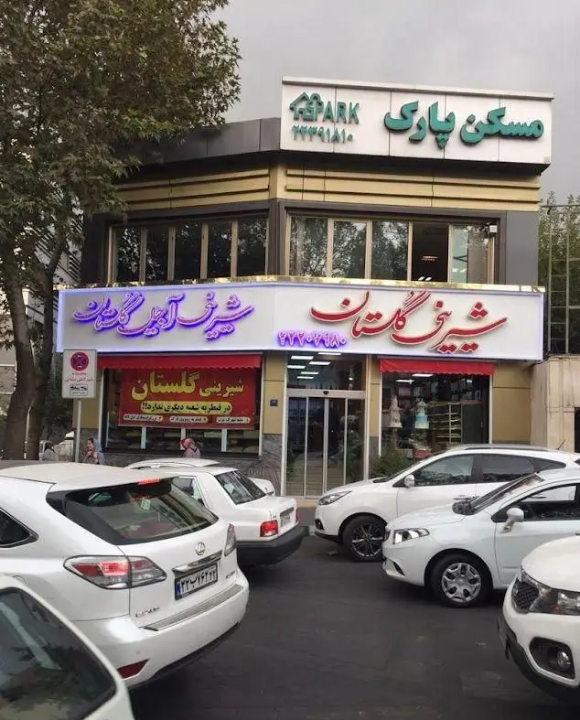 فروشگاه شیرینی و آجیل گلستان با تابلوی نئون جذاب و نمای دو طبقه، ارائه دهنده بهترین شیرینی‌ها و آجیل تازه برای مشتریان.