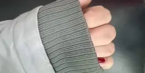 نمای نزدیک از کشباف سرآستین کاپشن طوسی رنگ به همراه ناخن با لاک قرمز تیره، مناسب برای ایده استایل زمستانی و پاییزه شیک