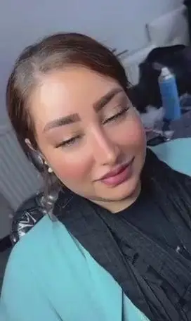 آرایش ملایم و شیک صورت زن جوان با سایه چشم درخشان و رژ لب صورتی ملایم همراه با شال مشکی و کت روشن در سالن زیبایی
