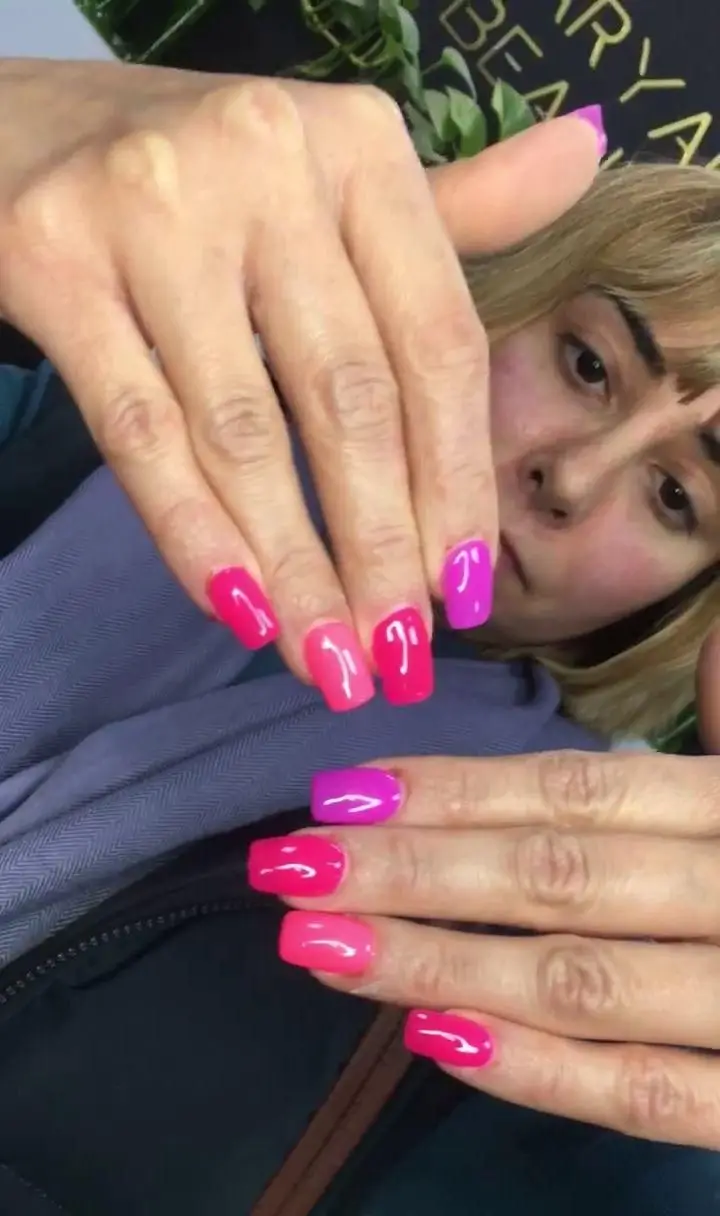 طراحی و کاشت ناخن دخترانه شیک با لاک ژل‌های براق در طیف‌های رنگی صورتی، سرخابی و بنفش در سالن زیبایی و آرایشی مریم بیوتی