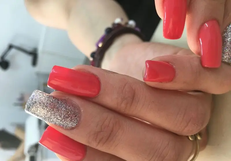 کاشت ناخن شیک با لاک قرمز مرجانی جذاب و یک ناخن طراحی شده با اکلیل نقره‌ای درخشان مناسب برای استایل‌های مجلسی و خاص