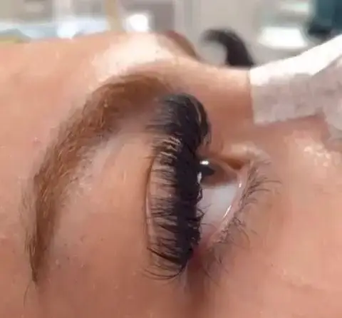 تصویر نمای نزدیک از فرآیند اجرای اکستنشن مژه والیوم مشکی و پرپشت بر روی مژه‌های چشم مشتری در مرکز زیبایی مریم موسوی