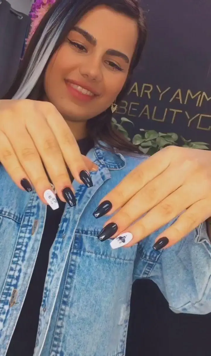 خانمی خندان با ناخن‌های بلند و طراحی شده به رنگ مشکی و سفید. طرح‌های هنری روی برخی ناخن‌ها و ژاکت جین او، استایلی مدرن و جذاب را به نمایش می‌گذارد.