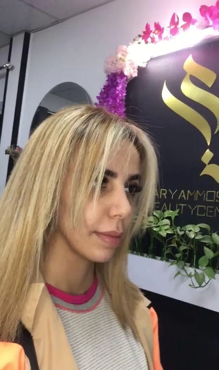 چهره زن جوان با رنگ موی بلوند روشن و صاف همراه با چتری در سالن زیبایی مریم موسوی با دکوراسیون گل‌های بنفش و صورتی