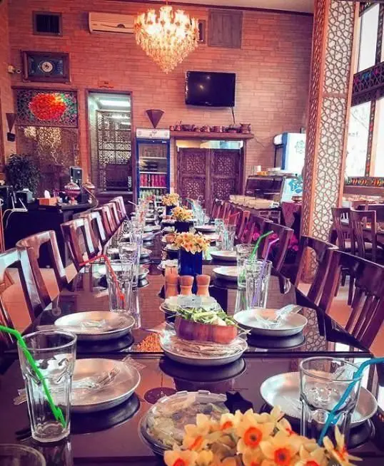 نمای دلنشین و دنج از فضای داخلی رستوران خوان باشی با دکوراسیون سنتی، میزهای بلند چیده شده آماده پذیرایی از مشتریان برای یک تجربه غذایی بی‌نظیر.